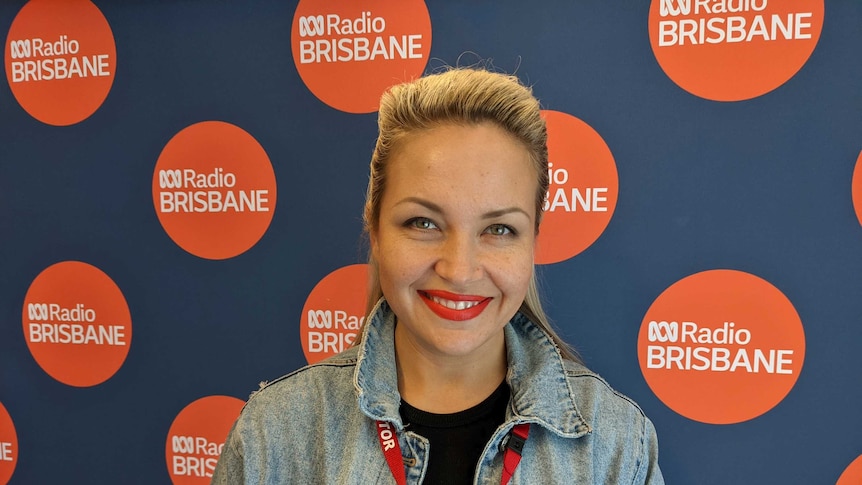 Natasha Petrova smiles as she stands in front of ABC Radio Brisbane banner