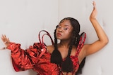 Press shot of Sampa The Great. Sampa is dressed in red, leaning against a white wall.