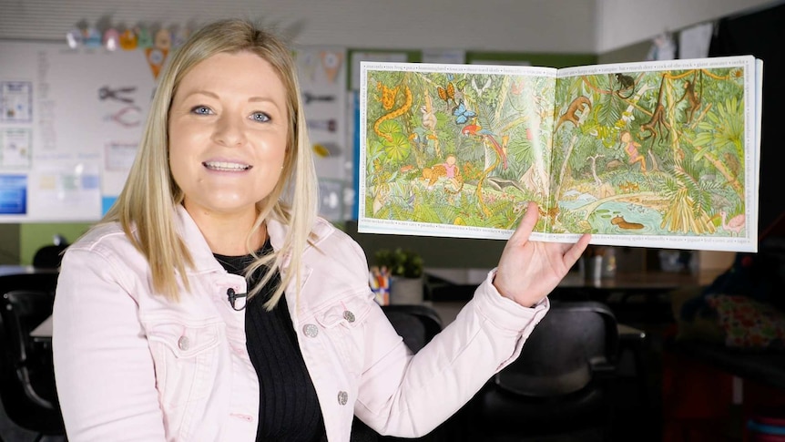 Female teacher holds up open picture book