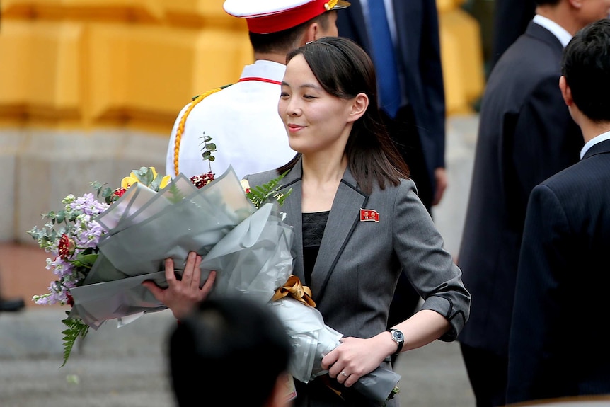 Kim Yo-jong smirking while holding a bunch of flowers