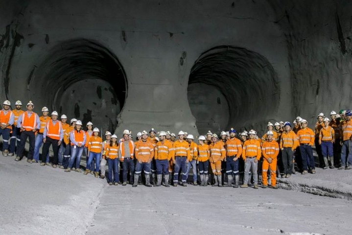 A large sweeping image shows construction workers in orange hi-vis who are made miniscule by underground rail lines.