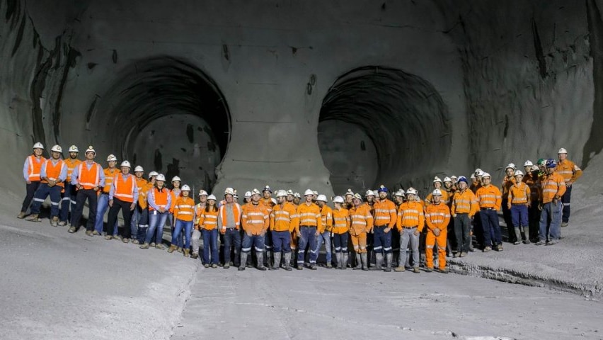 A large sweeping image shows construction workers in orange hi-vis who are made miniscule by underground rail lines.