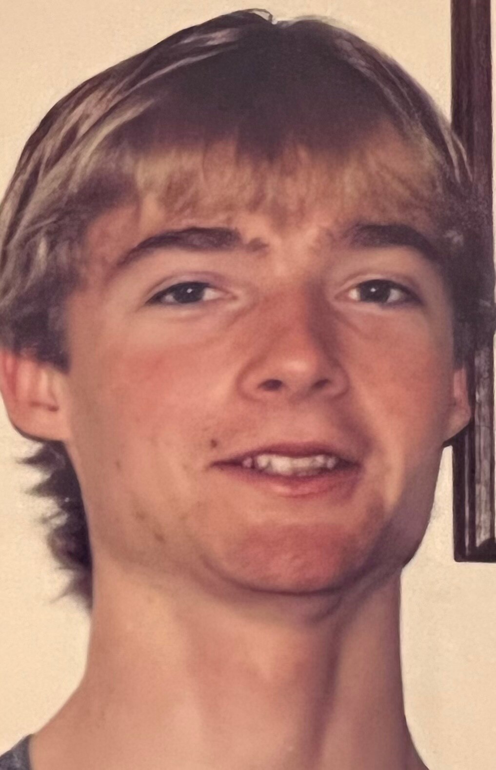 A boy with shaggy blonde hair smiles into the camera.