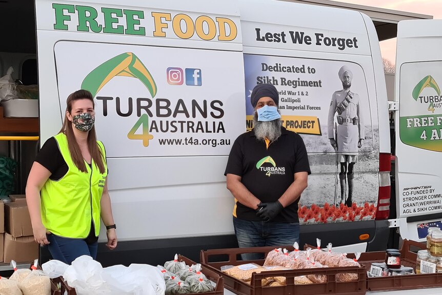Amar and a female volunteer in front of their truck, wearing masks, handing out food.