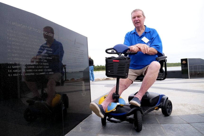 Man sits on mobility scooter near a black memorial wall