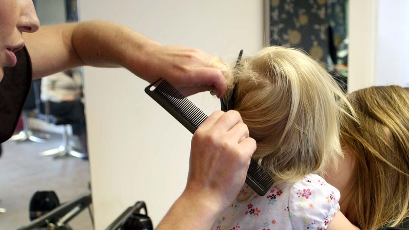 A hairdresser cuts the hair of a young child