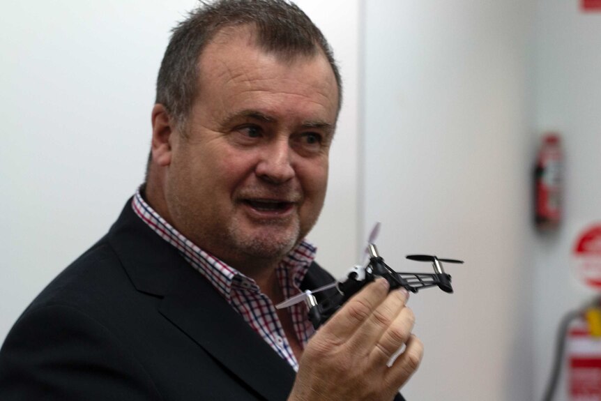 Former Victorian police detective Stephen Wilson holds a small drone in a classroom.