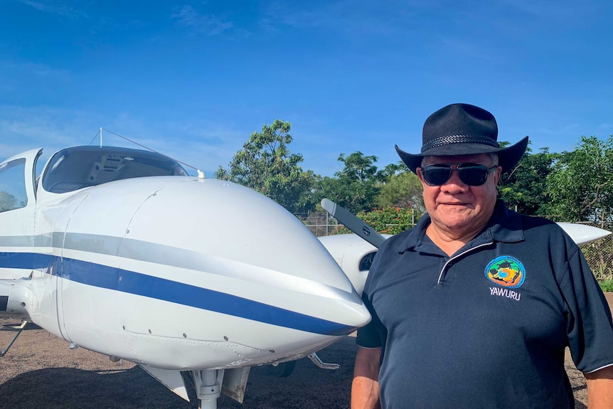 Mick Dodson wearing an Akubra hat and sunglasses, standing next to a light aircraft in the Northern Territory.