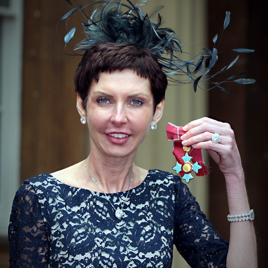 A woman holds up her Commander of the British Empire medal.