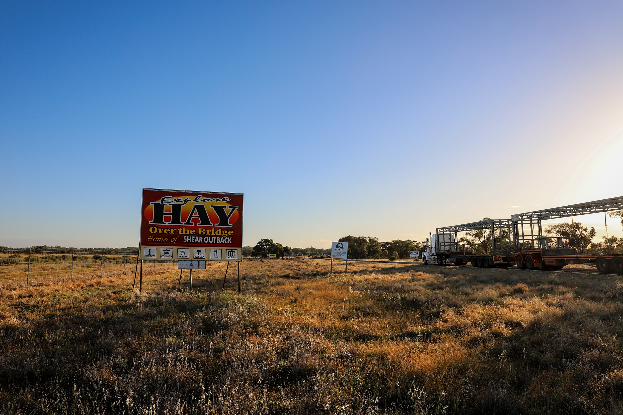 A sign that reads Explore Hay stands by the roadside as a truck passes at sunrise