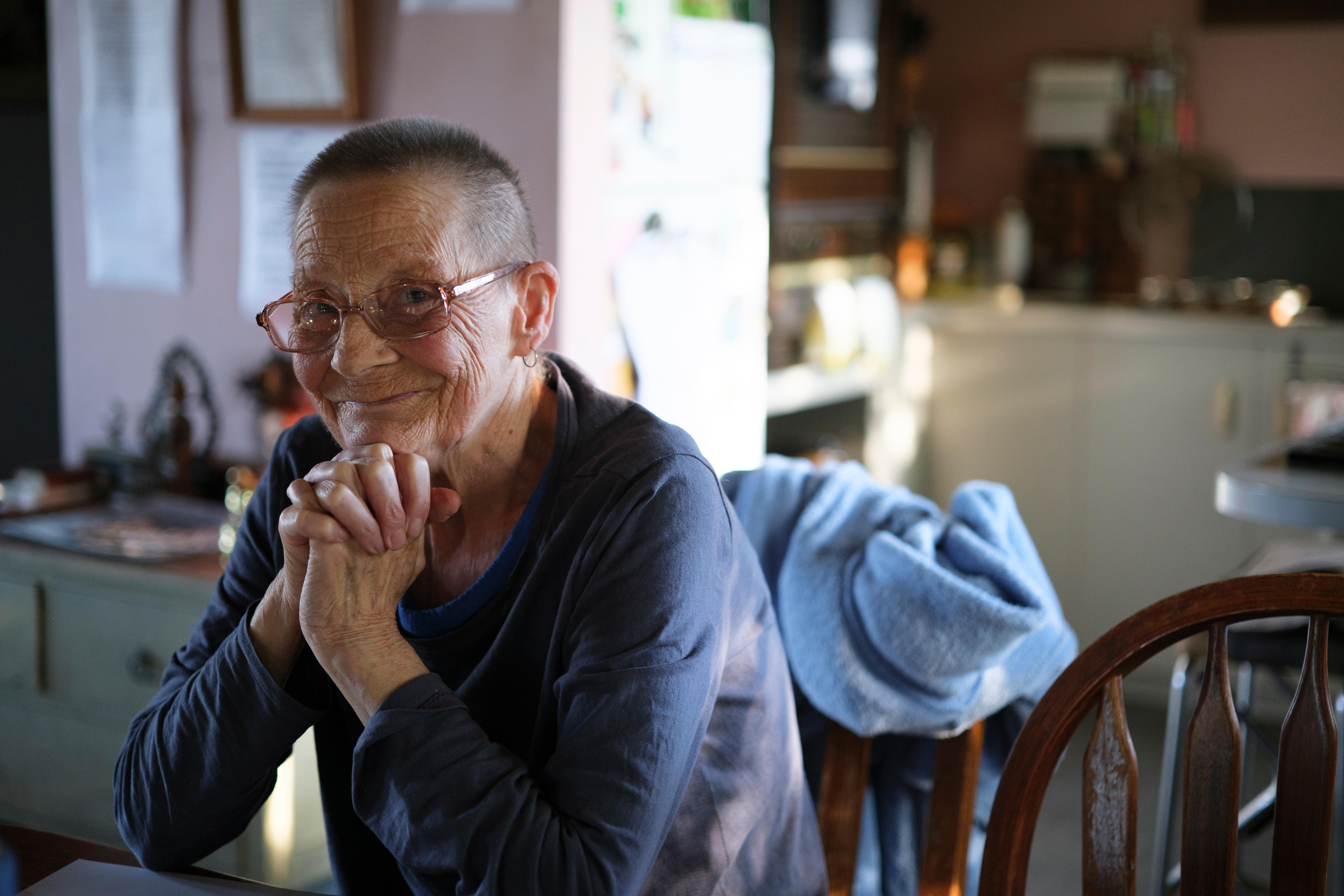 Deb smiles at the camera with her hands clasped together under her chin with elbows resting on the table.