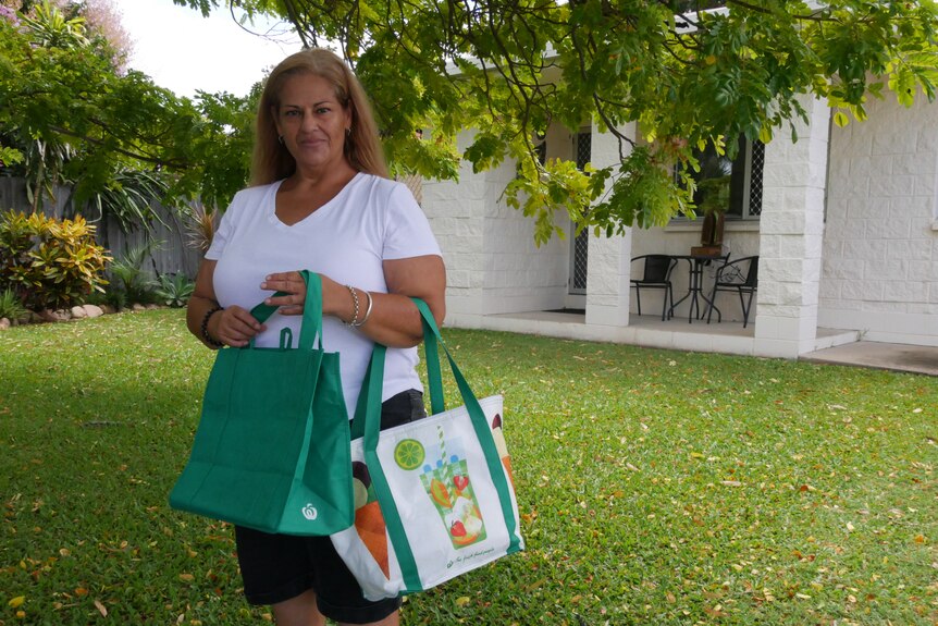 woman in white shirt holds two grocery bags