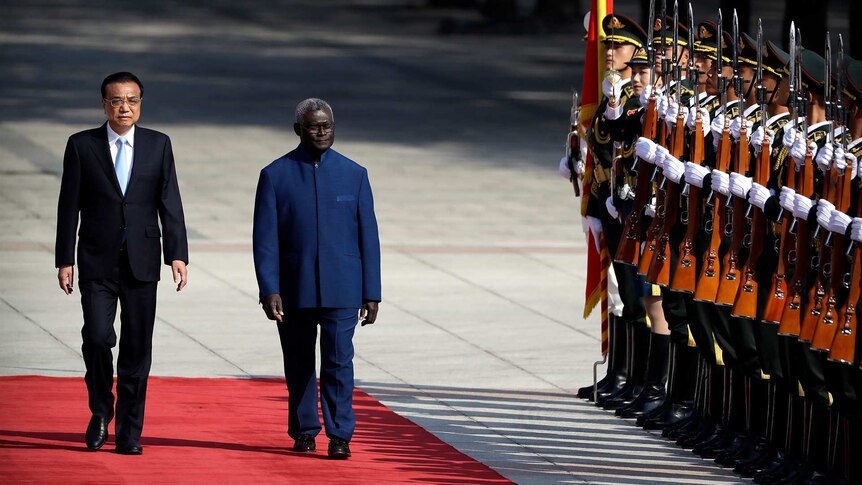 Solomon Islands Prime Minister Manasseh Sogavare walking past a line of military personnel.