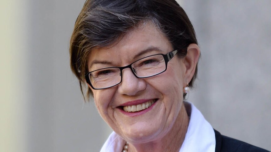 Cathy McGowan smiles at the camera while standing against a wall.