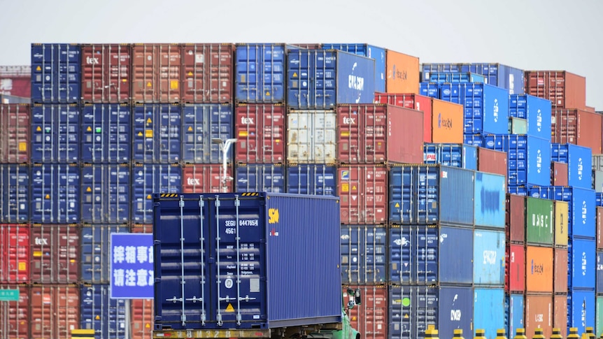 A green truck transports a blue shipping container at a cargo terminal in China