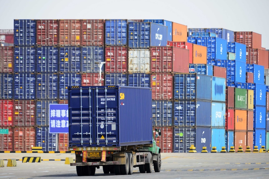 A green truck transports a blue shipping container at a cargo terminal in China