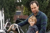A man sitting on a stationary motorbike with a toddler perched in front of him.