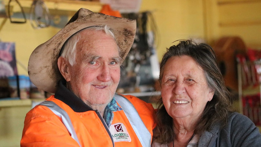 Play Audio. Elderly man in worn out and dirty Akubra hat & high vis orange jacket stands smiling with his arm around smiling elderly woman. Duration: 8 minutes 20 seconds