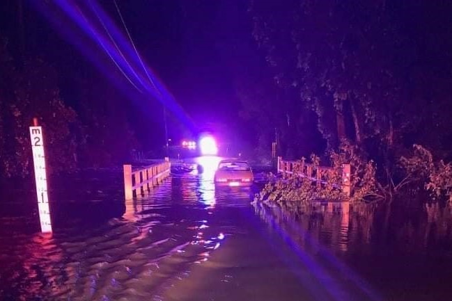 A car trapped in floodwaters on a bridge at night.