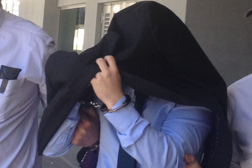 Massage therapist Marcello Scariati, handcuffed and with a jacket over his head, is escorted from a Perth court.