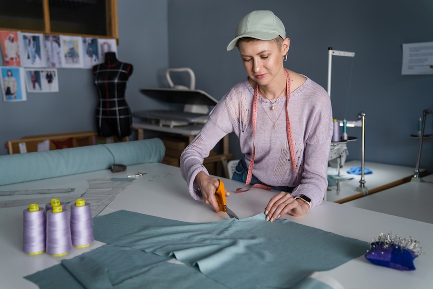 Barbara leans over a large craft table cutting fabric