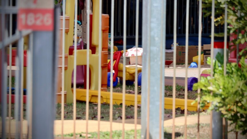 Plastic playground equipment in the front yard of a childcare centre, seen through a metal fence.