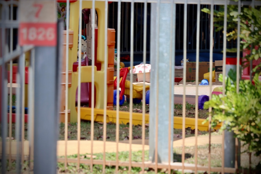 Plastic playground equipment in the front yard of a childcare centre, seen through a metal fence.