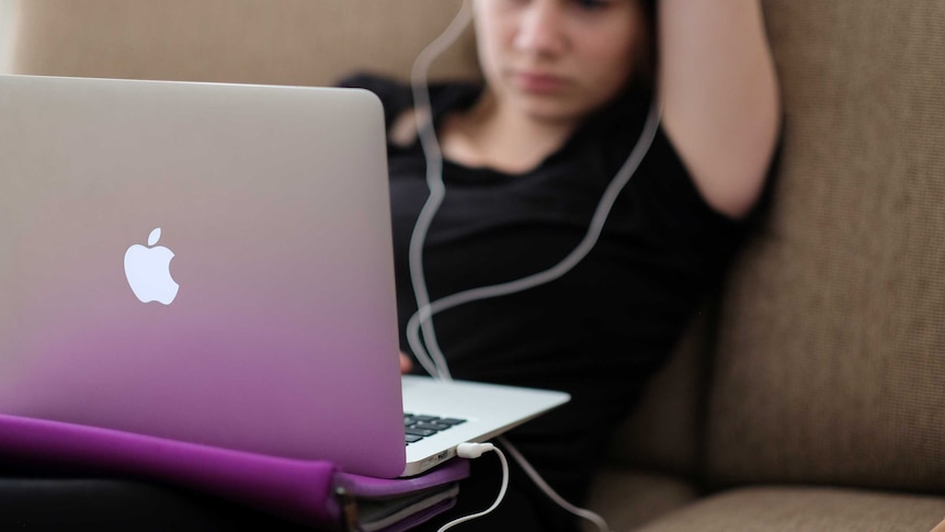 A woman sits on a couch watching a laptop with headphones in.