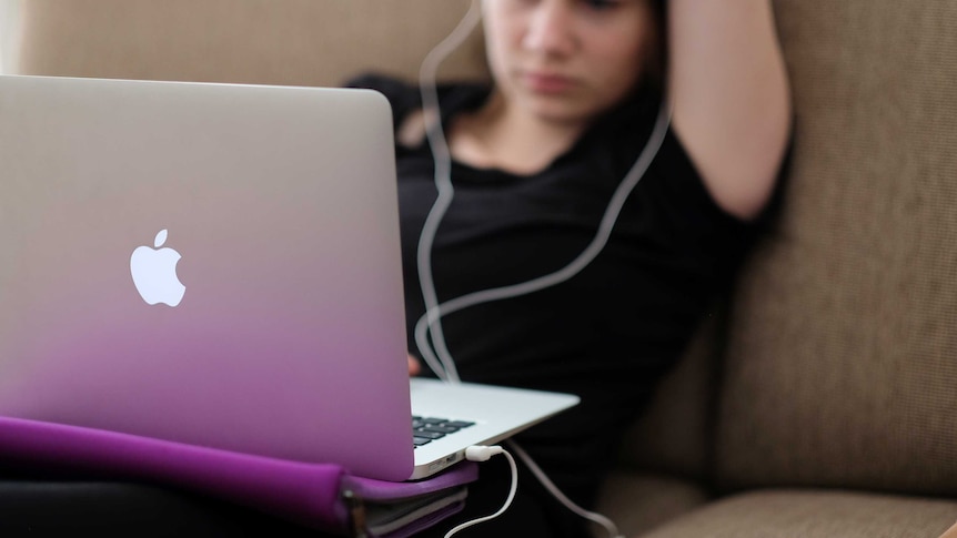A teenager uses a laptop computer sitting on a couch.