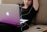 A woman sits on a couch watching a laptop with headphones in.
