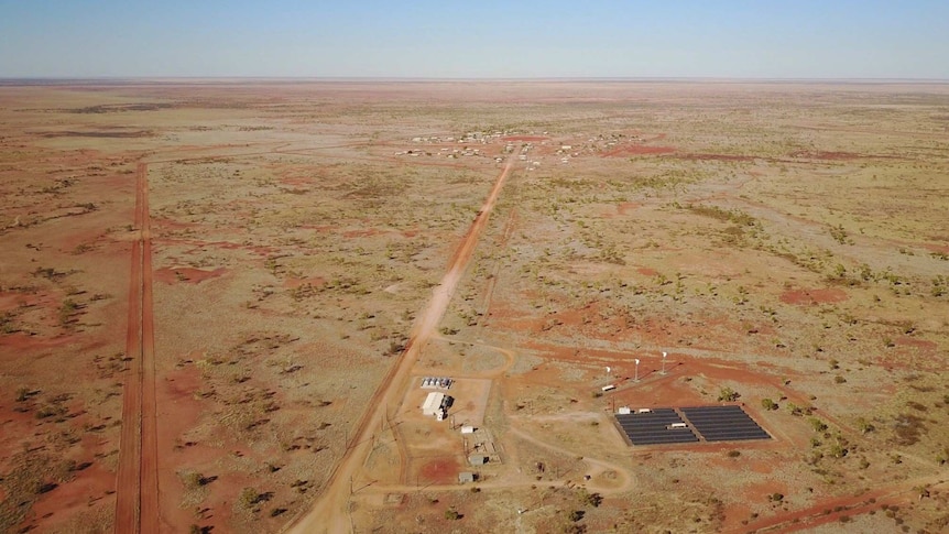 A wide drone shot of the solar farm with the community in the distance.