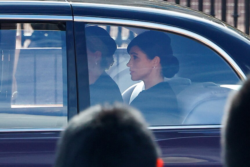 Duchess of Sessex Meghan in the back of a car wearing black. 