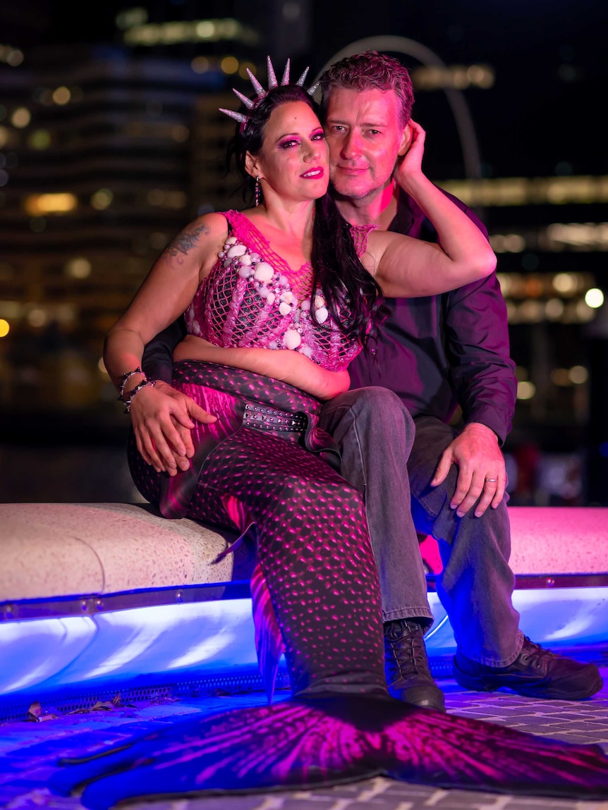 A man and a woman in a tail, sitting near a pool at night.