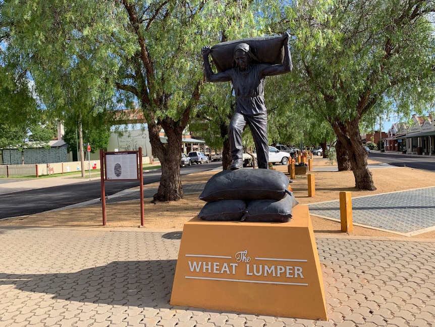 A bronze statue of a man carrying a bag of wheat on his back.