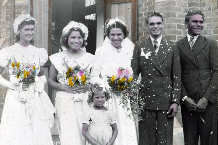 Three brides, two groomsmen and a flower girl smiling outside a church in the 1950s.