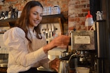 A young woman in a white shirt making a coffee at a coffee machine.