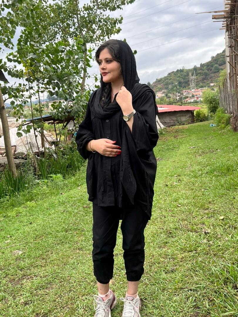 A photos of a young woman in black with loose headscarf staring off camera