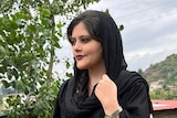 A photos of a young woman in black with loose headscarf staring off camera