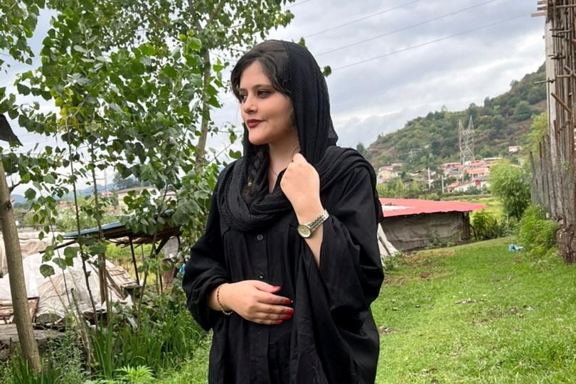 A photo of a young woman in black with loose headscarf staring off camera