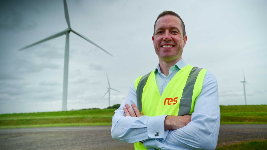 A man in a high vis vest standing in front of wind turbines