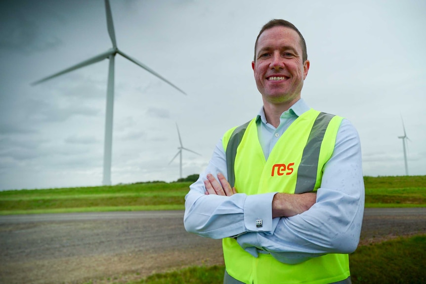 A man in a high vis vest standing in front of wind turbines