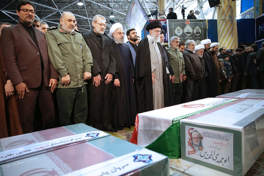 Men stand in a row midway through an Islamic prayer for slain general Qassem Soleimani.