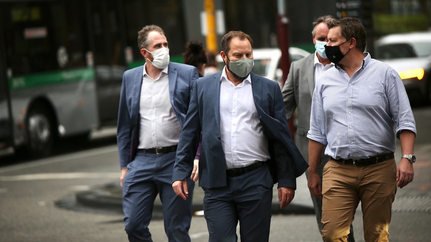 A line of men walking through Perth while wearing COVID masks