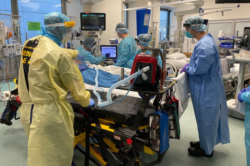 People wearing PPE gather around a hospital bed.