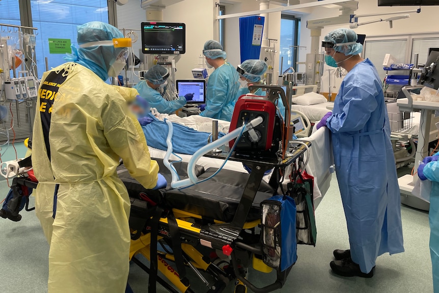 People wearing PPE gather around a hospital bed.