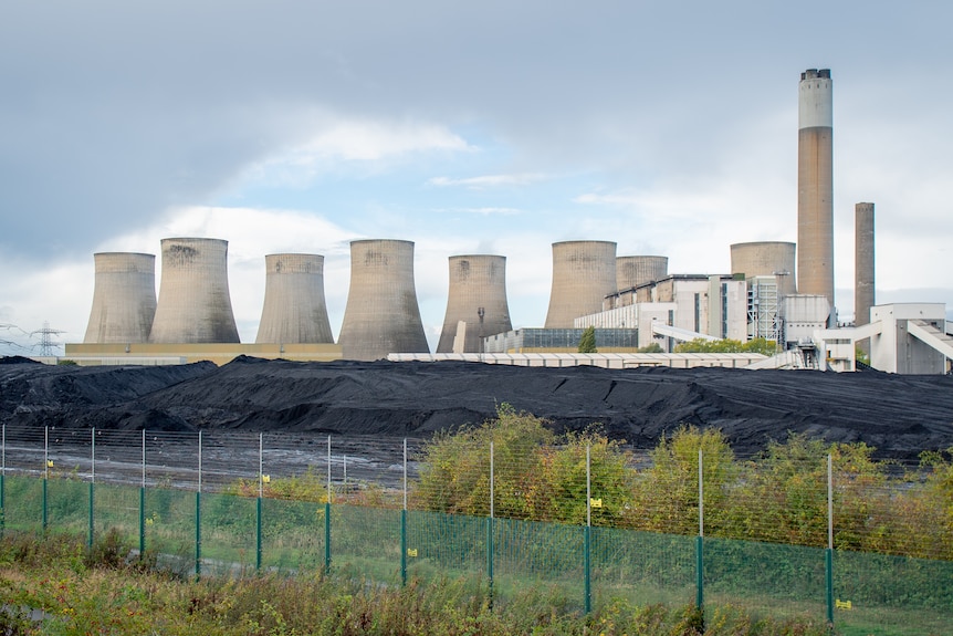 Mounds of coal sits in front of cooling stacks of a power station.