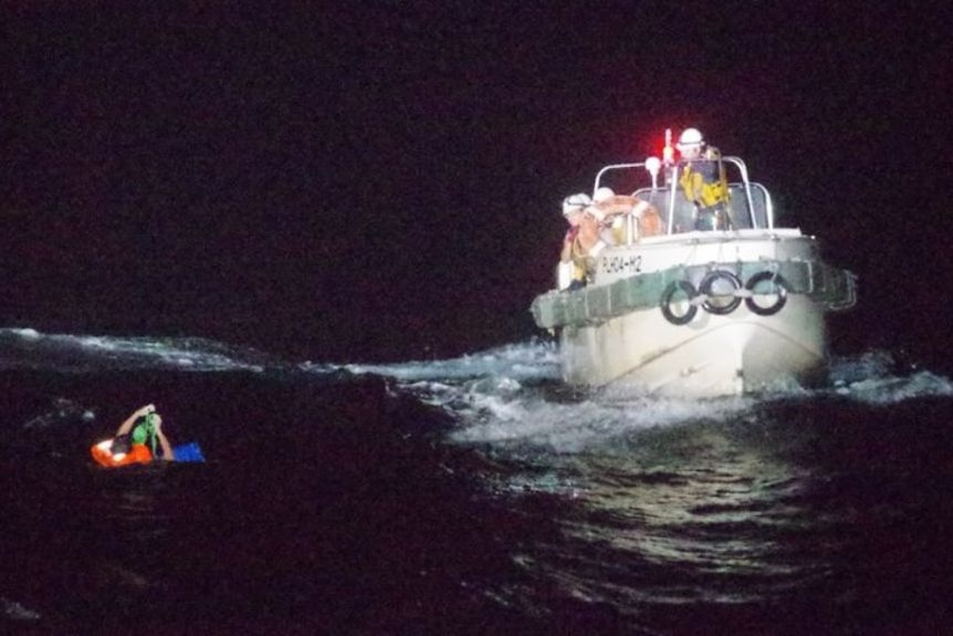 A rescue crew on a small vessel look at a man in the water.