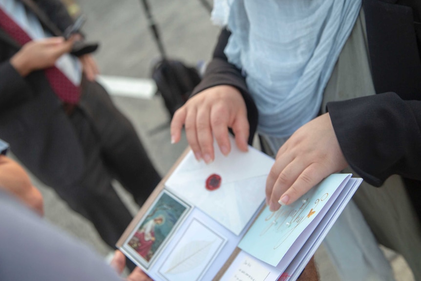 A woman's hands rest on a display book featuring condolence cards and messages for Aiia Maasarwe's loved ones.