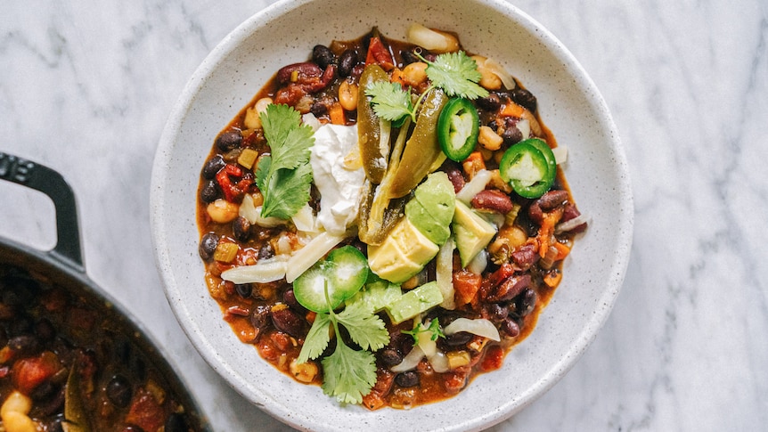 Bowl of vegetarian chilli topped with sour cream, avocado, coriander, jalapeno, a vegetarian dinner that freezes well.