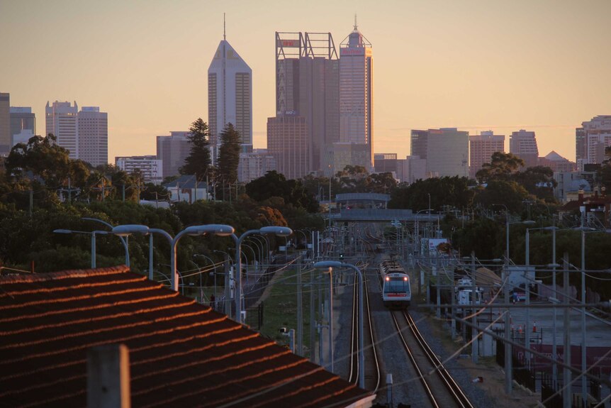 A train moves along a rail line leading directly to Perth city at sunset